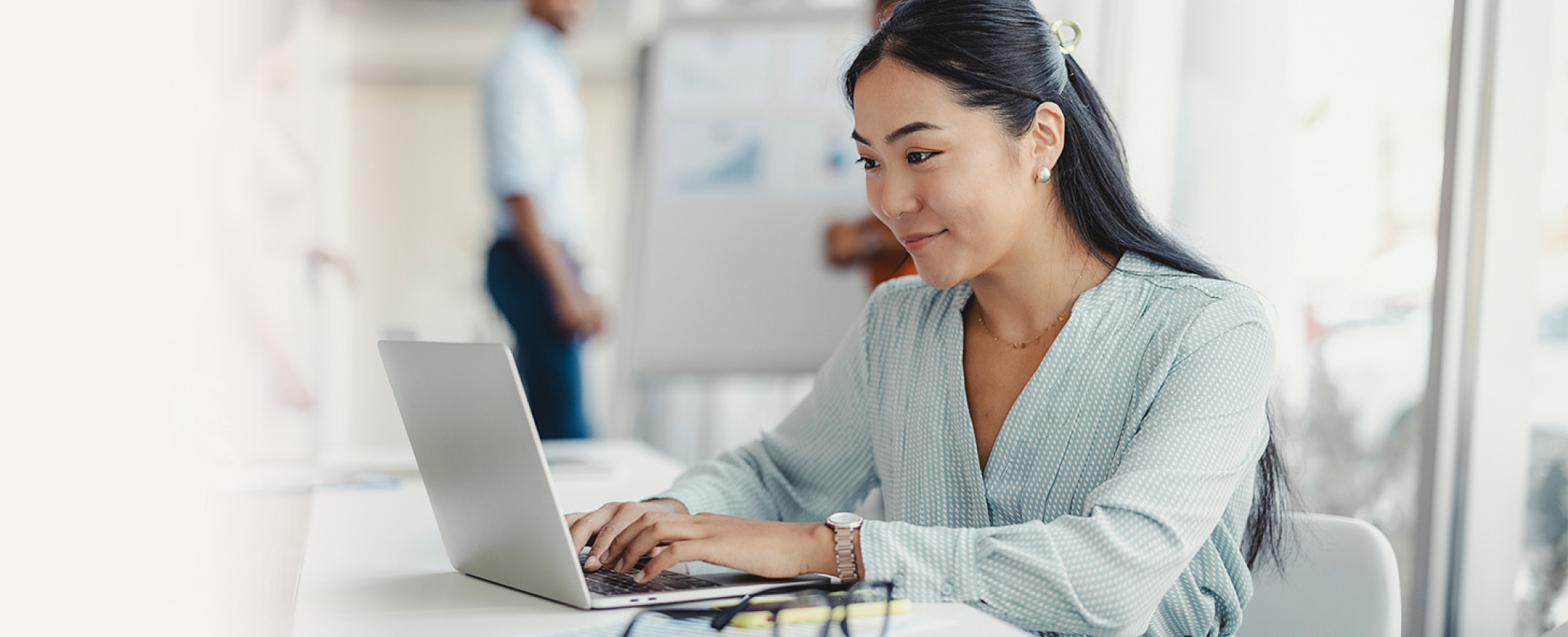 A woman sitting at a worktable uses a laptop.