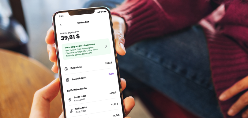 Une personne tient un t&eacute;l&eacute;phone intelligent affichant la page &laquo; Coffre-fort &raquo; du compte MonArgent Postes Canada offert avec Koho. 
