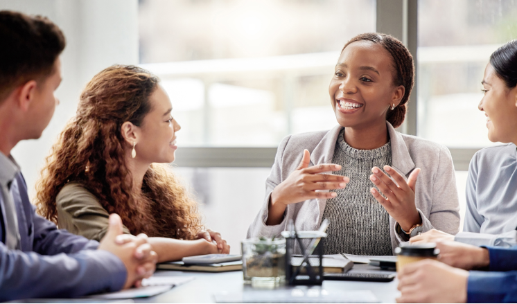 A group of people at a meeting table in a brightly lit office environment. 