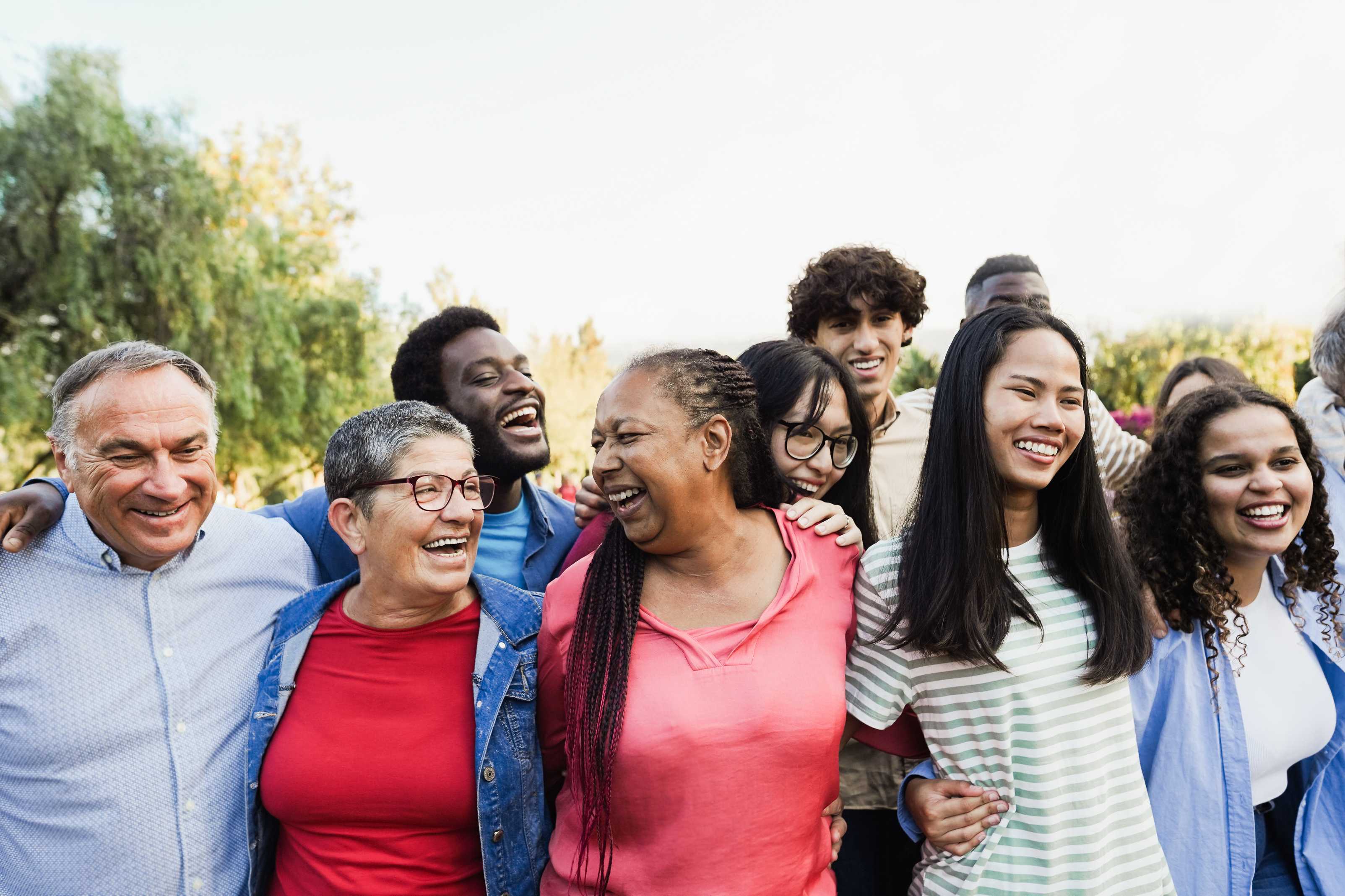 Un groupe diversifié de personnes qui sourient et rient en se rassemblant les bras autour des épaules.