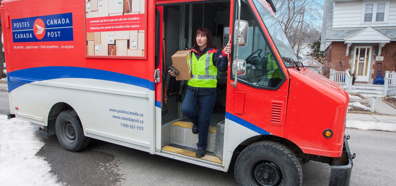 Agente de livraison sortant d’un camion de Postes Canada dans un quartier résidentiel pour livrer un colis