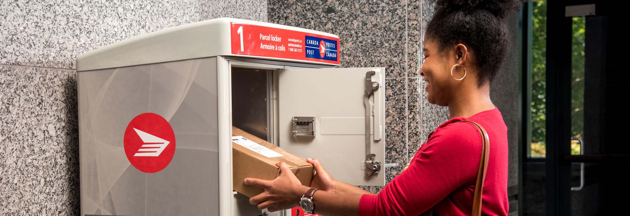 Une femme récupère son colis dans l’casier à colis de Postes Canada dans la salle de courrier de son immeuble d’habitation