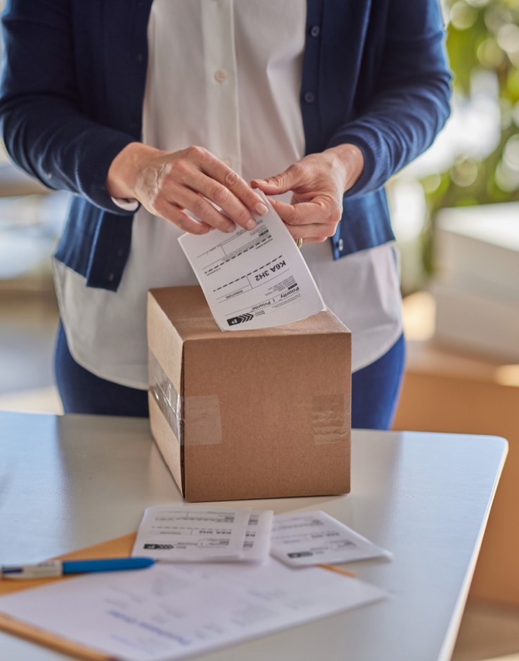 Une femme appose une étiquette de retour de Postes Canada sur le dessus d’un colis.